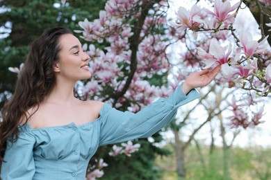 Photo of Beautiful woman touching blossoming magnolia tree branch on spring day