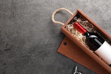 Bottle of wine in wooden box and corkscrew on dark textured table, flat lay. Space for text