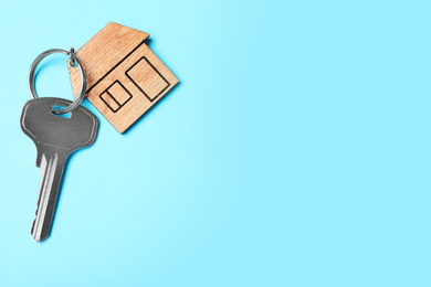 Photo of Key with trinket in shape of house on light blue background, top view and space for text. Real estate agent services