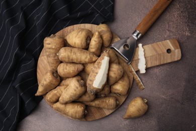 Photo of Tubers of turnip rooted chervil and peeler on brown table, top view