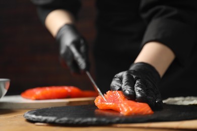 Photo of Chef in gloves cutting salmon for sushi at table, closeup