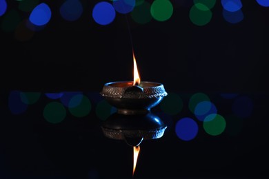 Photo of Lit diya on dark background with blurred lights. Diwali lamp