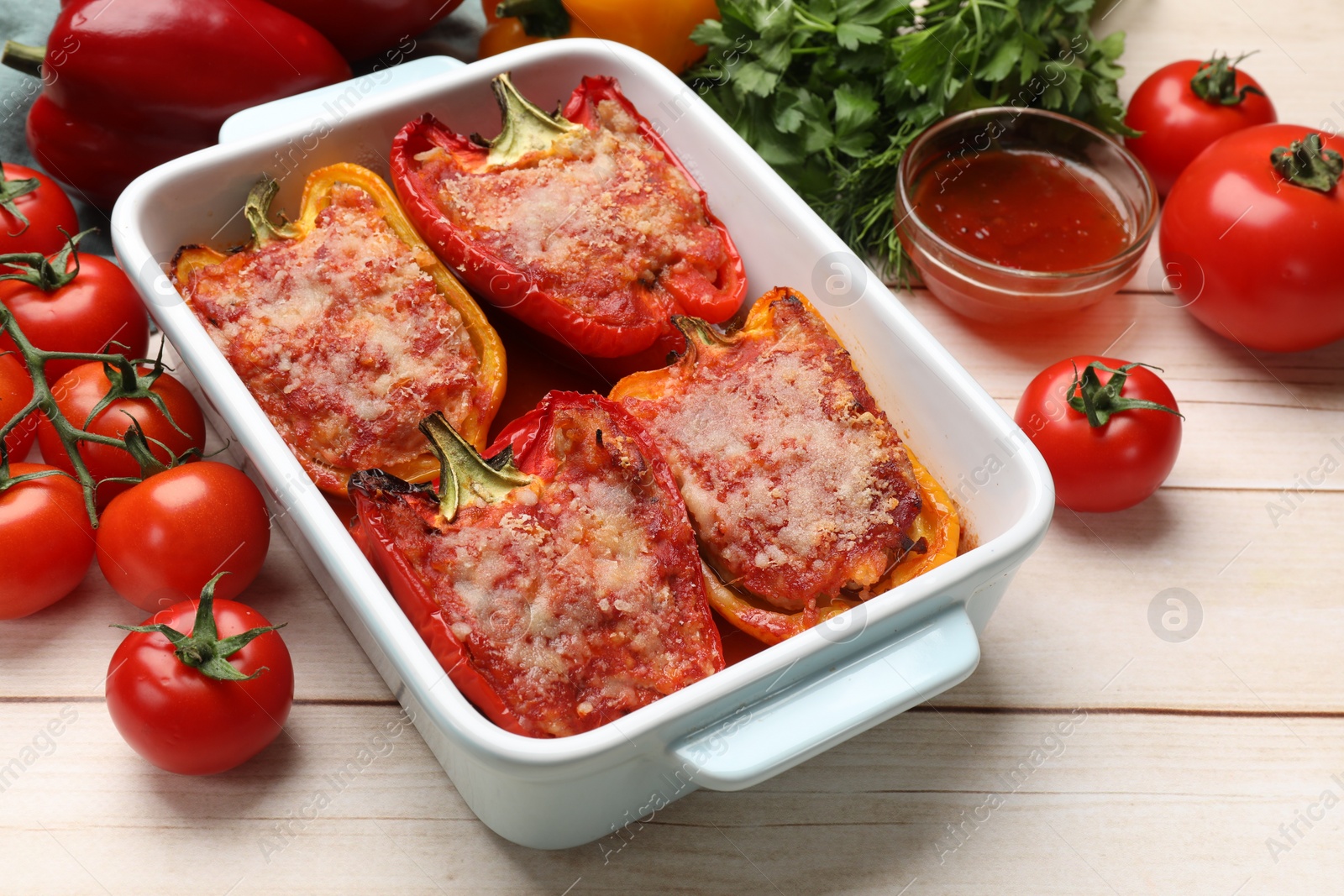 Photo of Tasty stuffed peppers in dish and ingredients on light wooden table