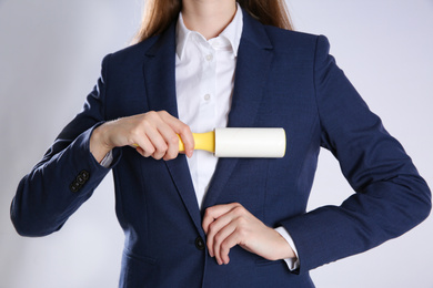 Photo of Woman cleaning dark blue jacket with lint roller on grey background, closeup