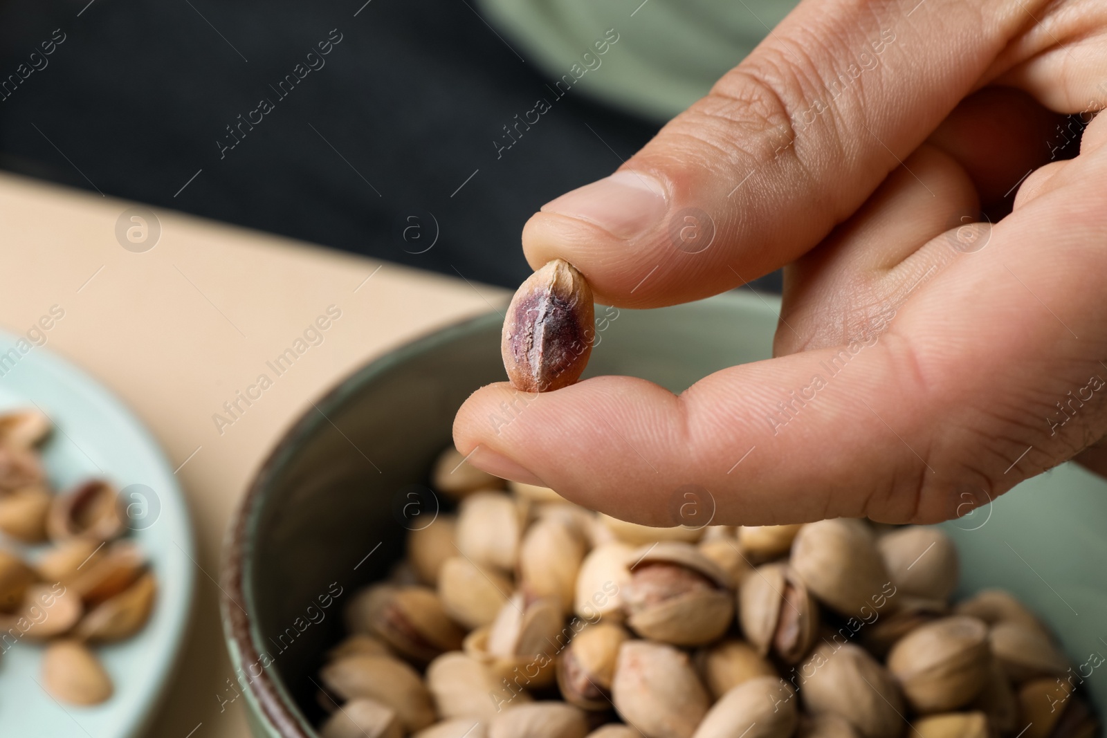 Photo of Woman holding tasty peeled pistachio nut over bowl, closeup