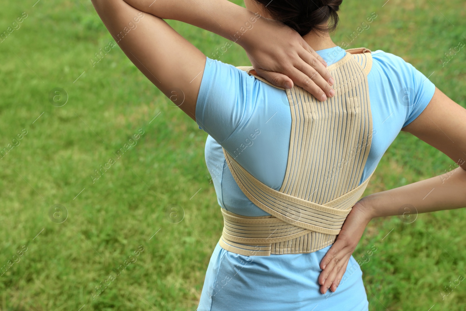 Photo of Closeup of woman with orthopedic corset on green grass outdoors, back view. Space for text