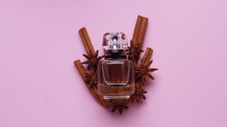Photo of Bottle of perfume, cloves and cinnamon sticks on pink background, top view
