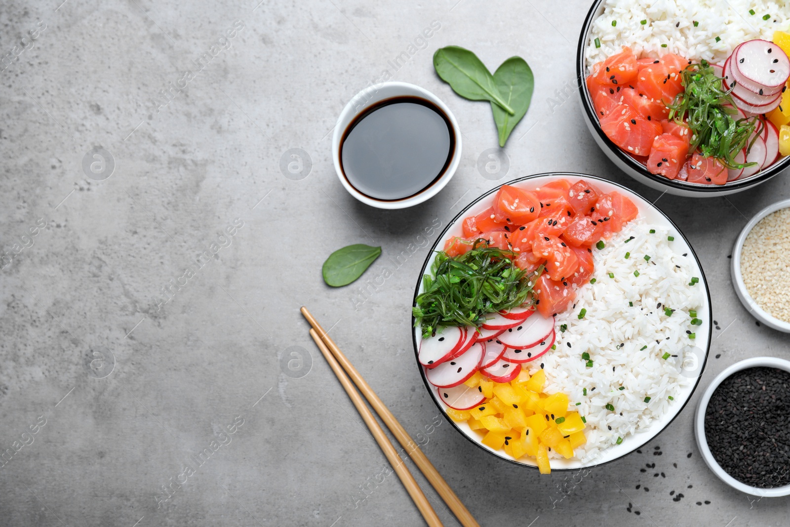 Photo of Delicious poke bowls with salmon and vegetables served on light grey table, flat lay. Space for text