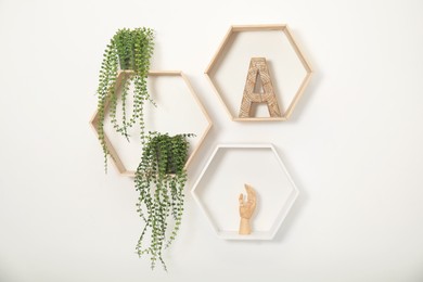 Photo of Honeycomb shaped shelves with decorative elements and houseplants on white wall