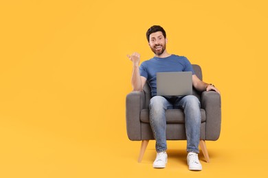 Photo of Emotional man with laptop sitting in armchair against yellow background. Space for text