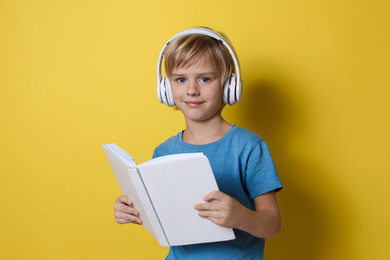 Photo of Cute little boy with headphones listening to audiobook on yellow background