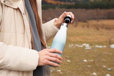 Woman holding thermo bottle and cap in mountains, closeup. Space for text