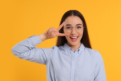 Beautiful woman in glasses showing V-sign on orange background