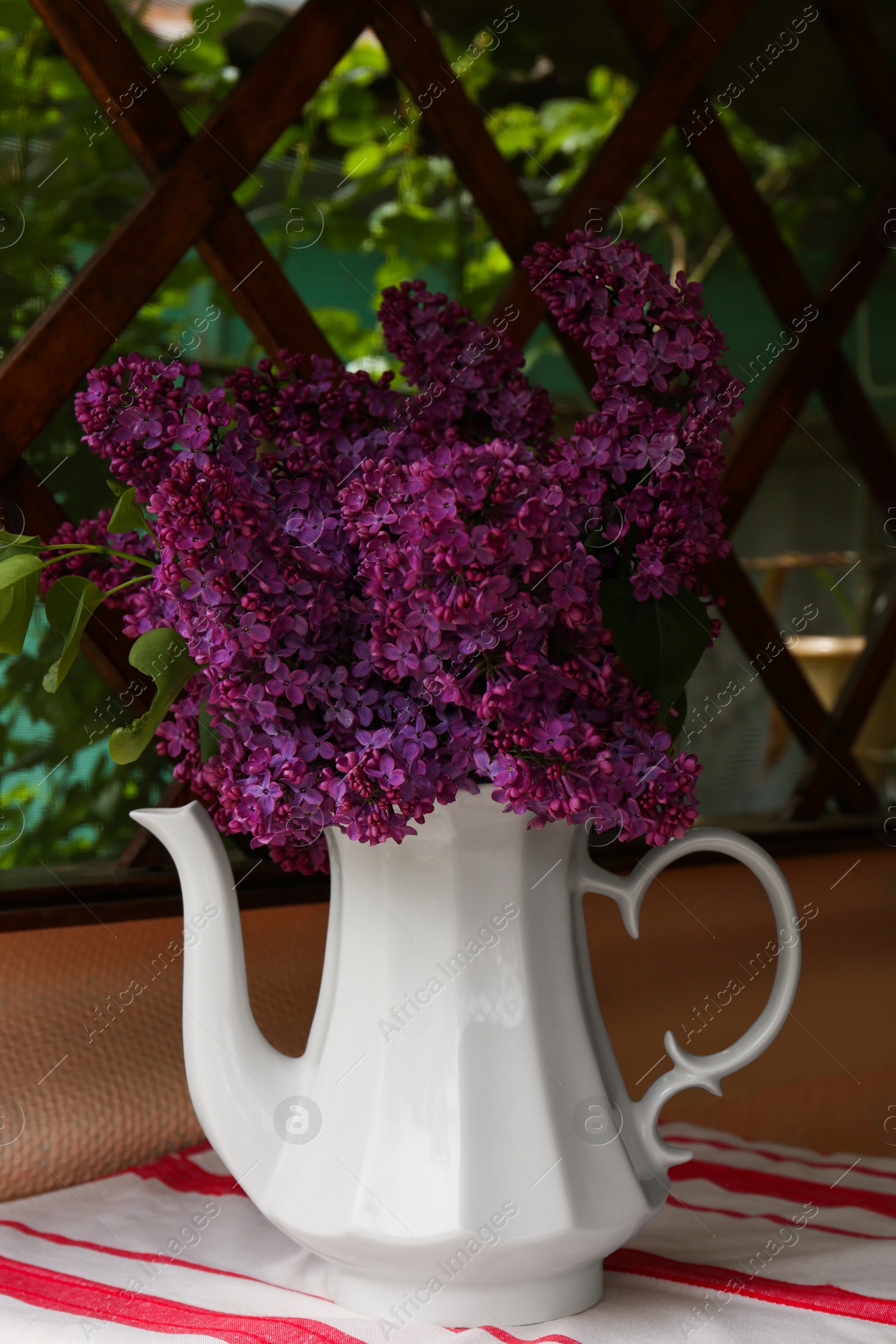 Photo of Beautiful lilac flowers in teapot near window indoors