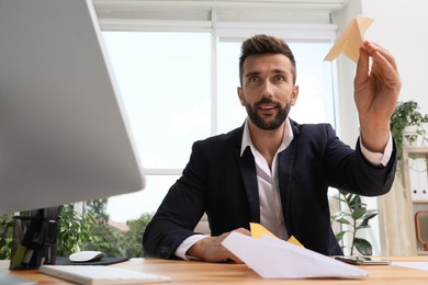 Handsome businessman playing with paper plane at desk in office