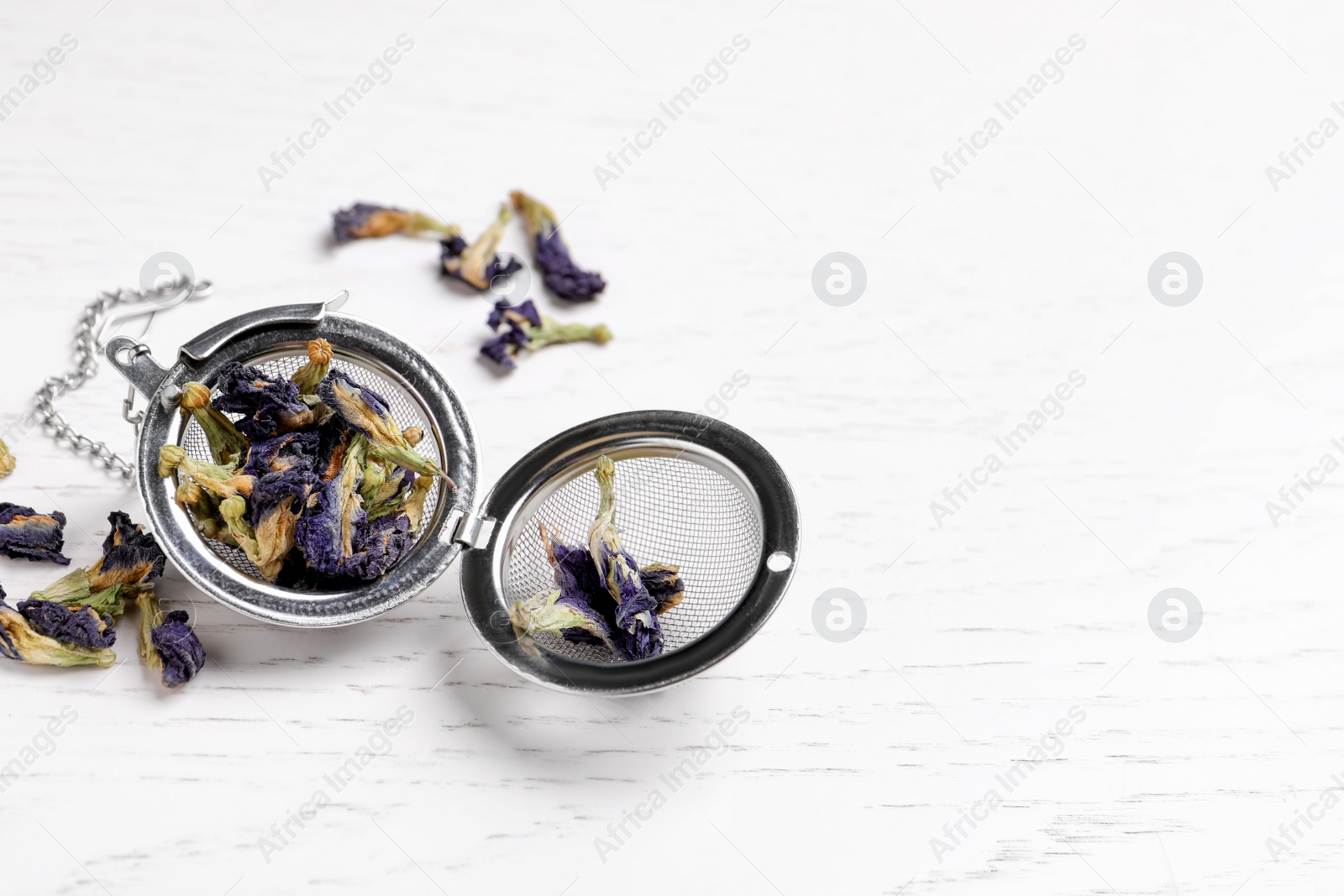 Photo of Dry organic blue Anchan and metal infuser on white wooden table, space for text. Herbal tea