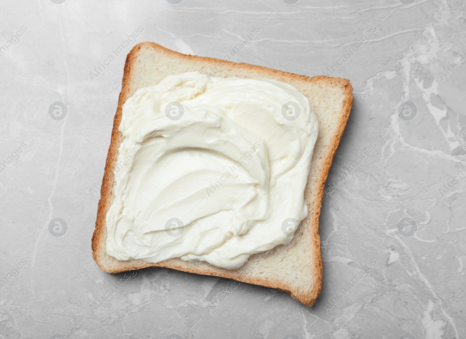 Photo of Slice of bread with tasty cream cheese on light grey marble table, top view