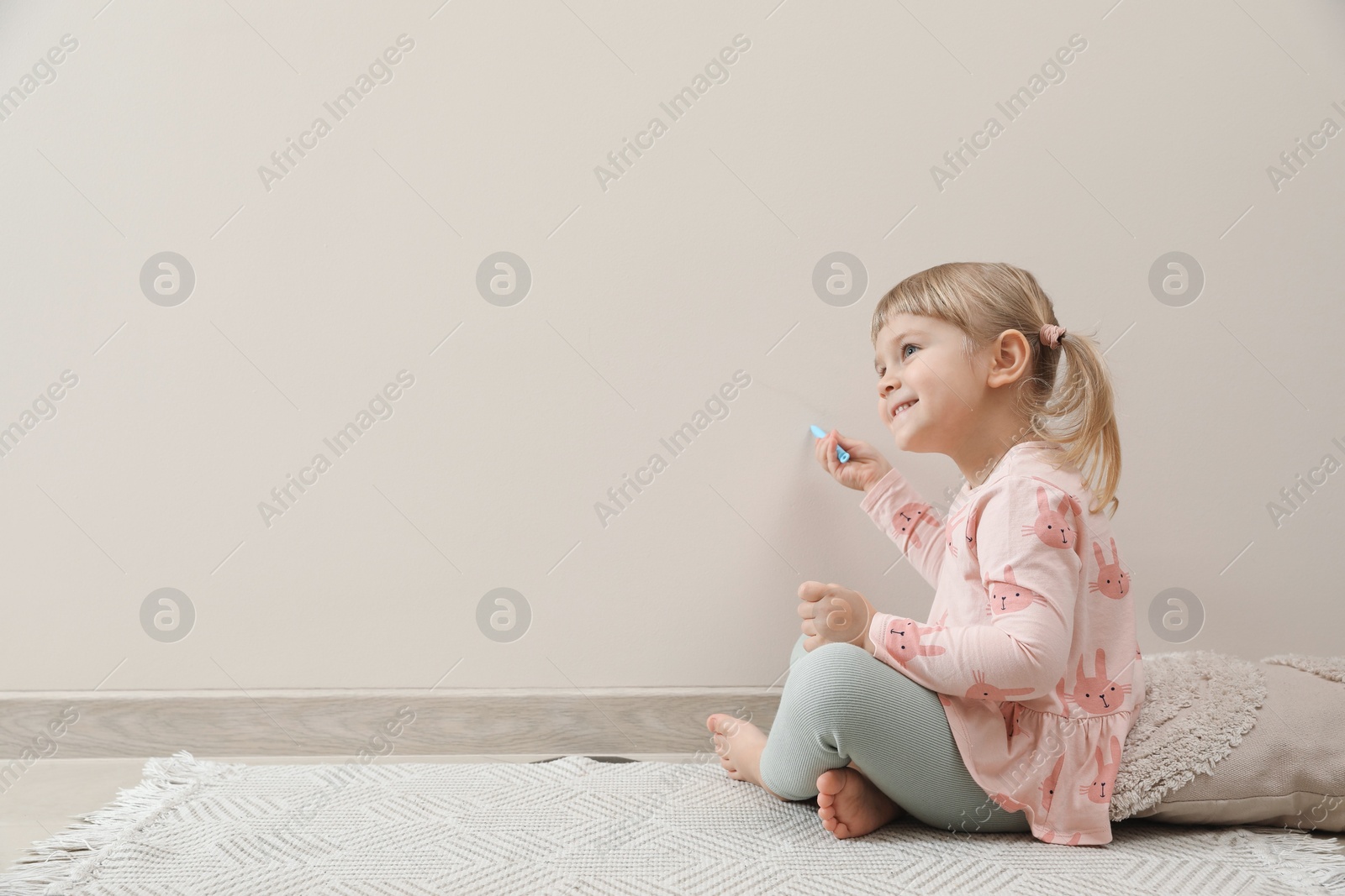 Photo of Little girl drawing on beige wall indoors, space for text. Child`s art