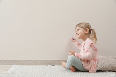 Little girl drawing on beige wall indoors, space for text. Child`s art