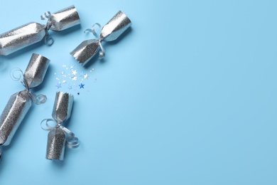 Open silver Christmas crackers with shiny confetti on light blue background, flat lay. Space for text
