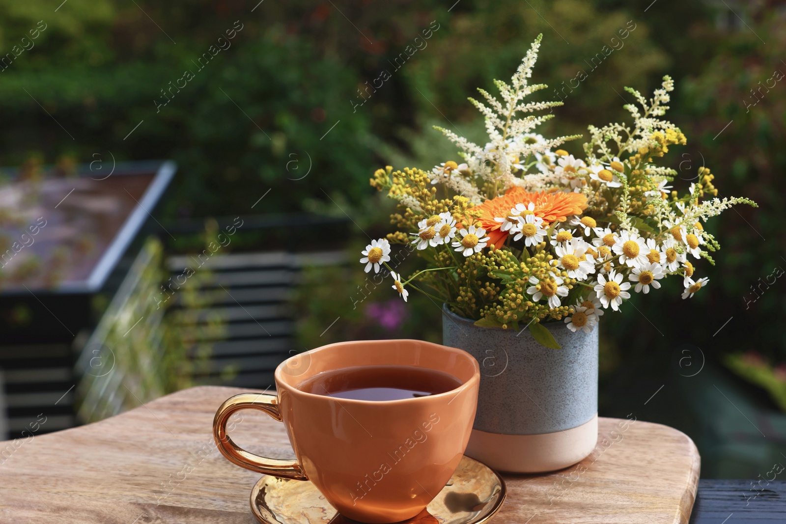 Photo of Cup of delicious chamomile tea and fresh flowers outdoors. Space for text