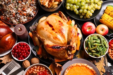 Photo of Traditional Thanksgiving day feast with delicious cooked turkey and other seasonal dishes served on black wooden table, flat lay