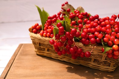 Photo of Wicker basket with ripe red viburnum berries on table, closeup