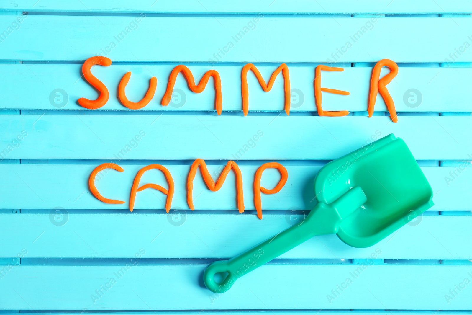 Photo of Flat lay composition with words SUMMER CAMP made from modelling clay and plastic shovel on color background