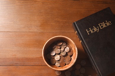 Photo of Donate and give concept. Coins in bowl and Bible on wooden table, flat lay. Space for text