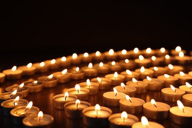 Burning candles on wooden table against black background