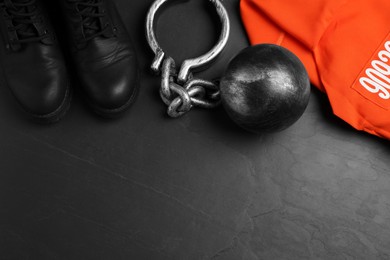 Photo of Prisoner ball with chain, jail clothes and boots on black table, flat lay. Space for text