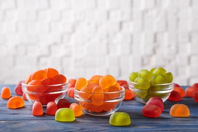 Glass bowls with tasty jelly candies on blue wooden table against white background, space for text