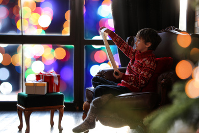 Photo of Little boy with wish list to Santa Claus near window indoors. Christmas holiday