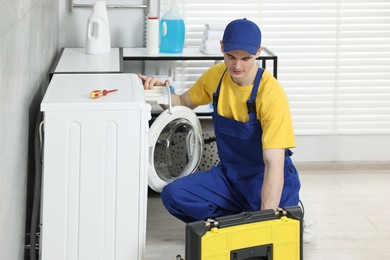 Young plumber repairing washing machine in bathroom