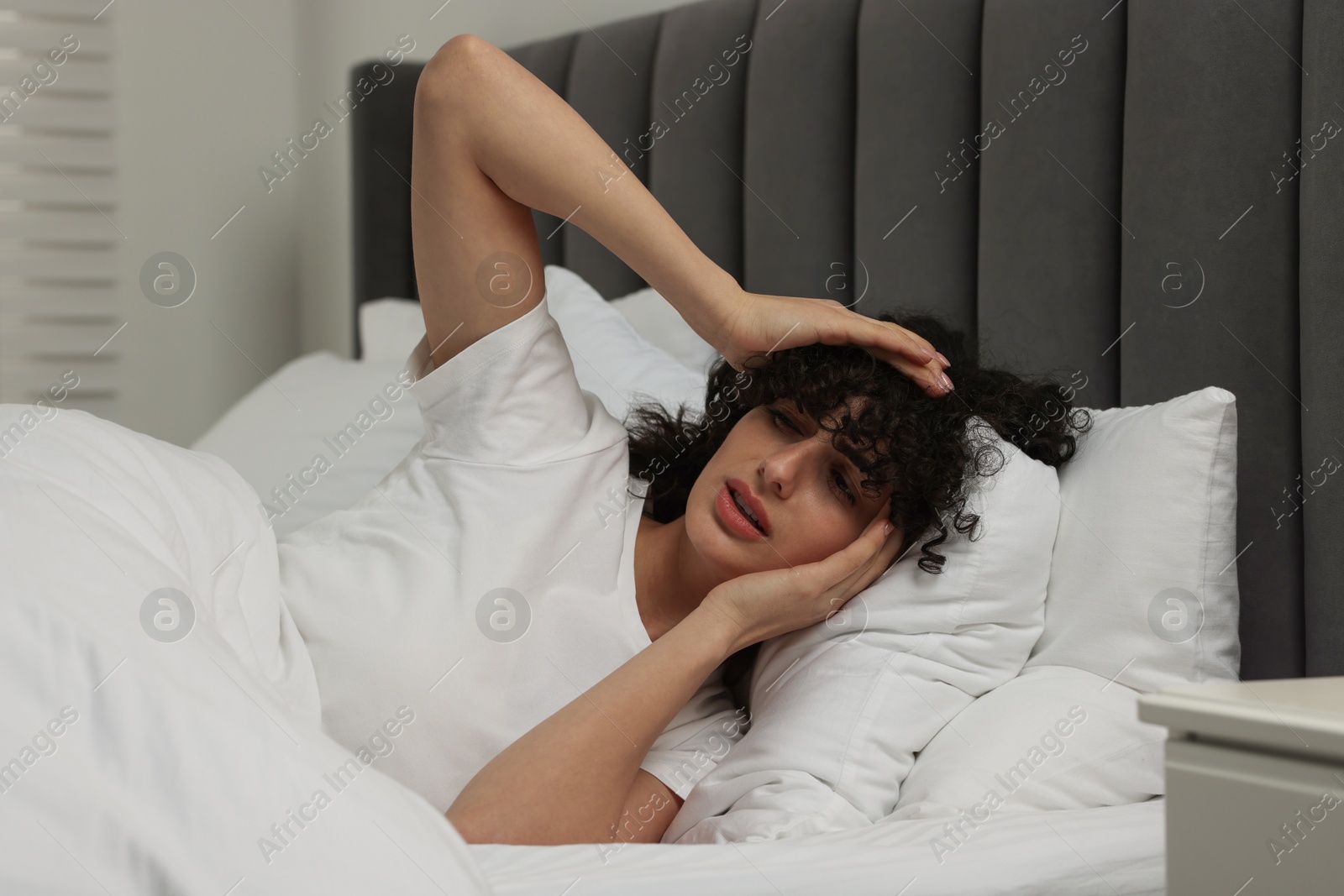 Photo of Young woman suffering from headache in bed at night