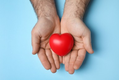 Man holding red heart on light blue background, top view