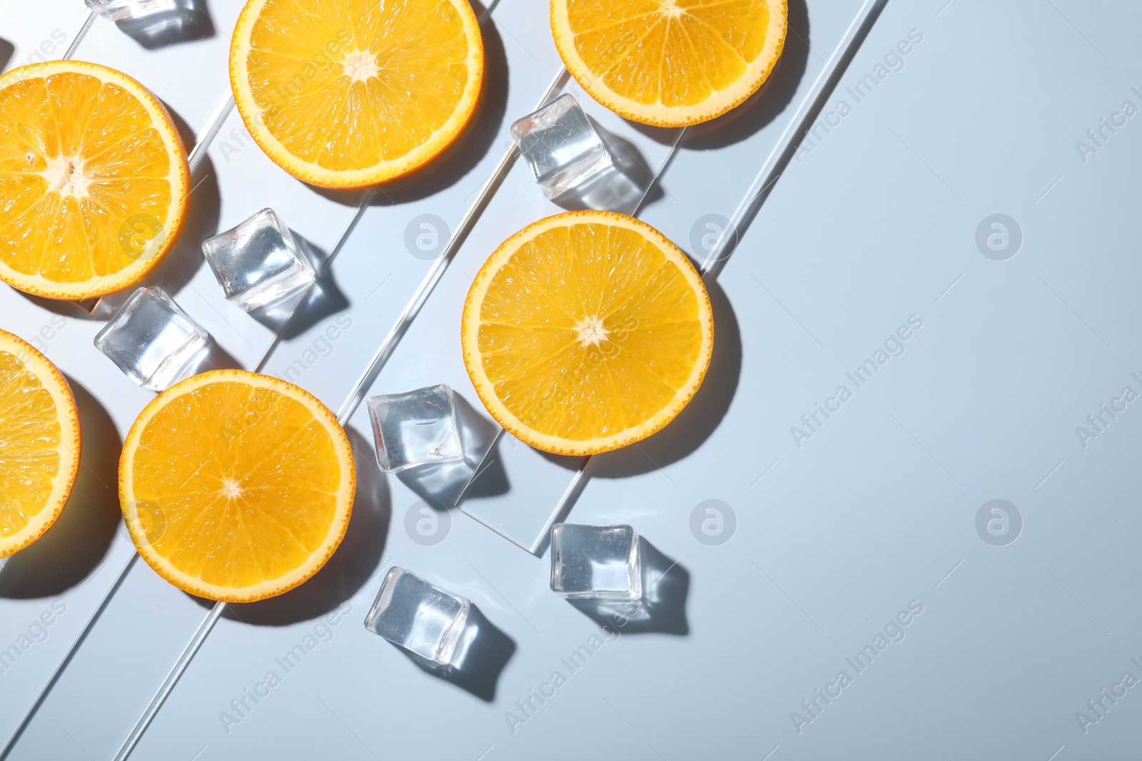 Photo of Slices of juicy orange and ice cubes on light blue background, flat lay. Space for text