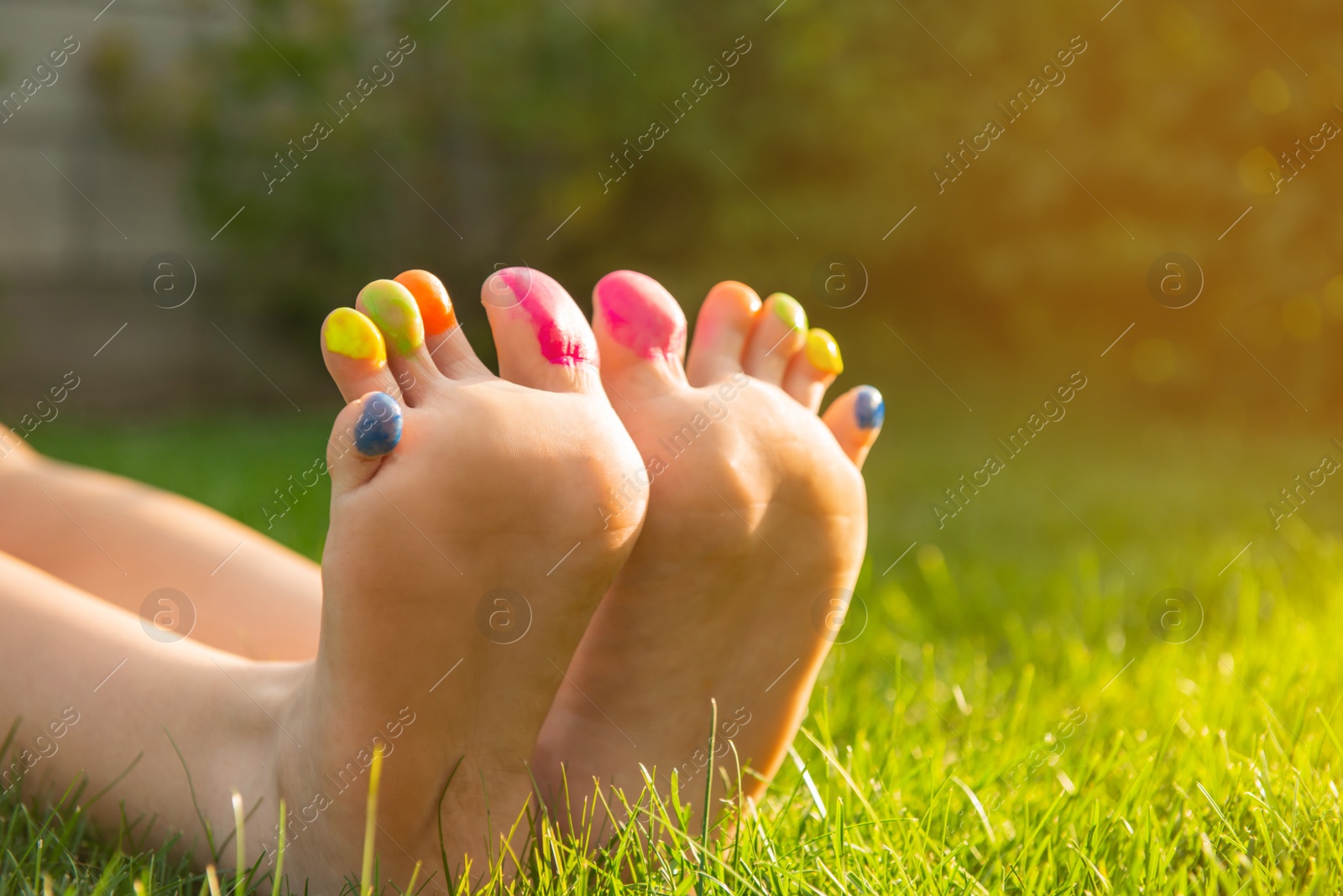 Photo of Teenage girl with painted toes on green grass outdoors, closeup