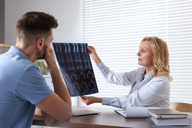 Photo of Doctor with MRI image consulting patient in clinic