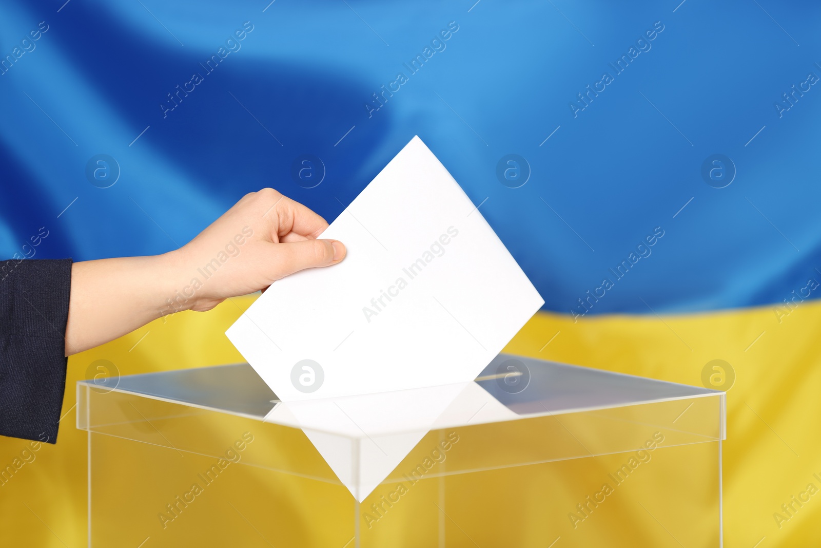 Photo of Woman putting voting paper into ballot box against Ukrainian flag, closeup