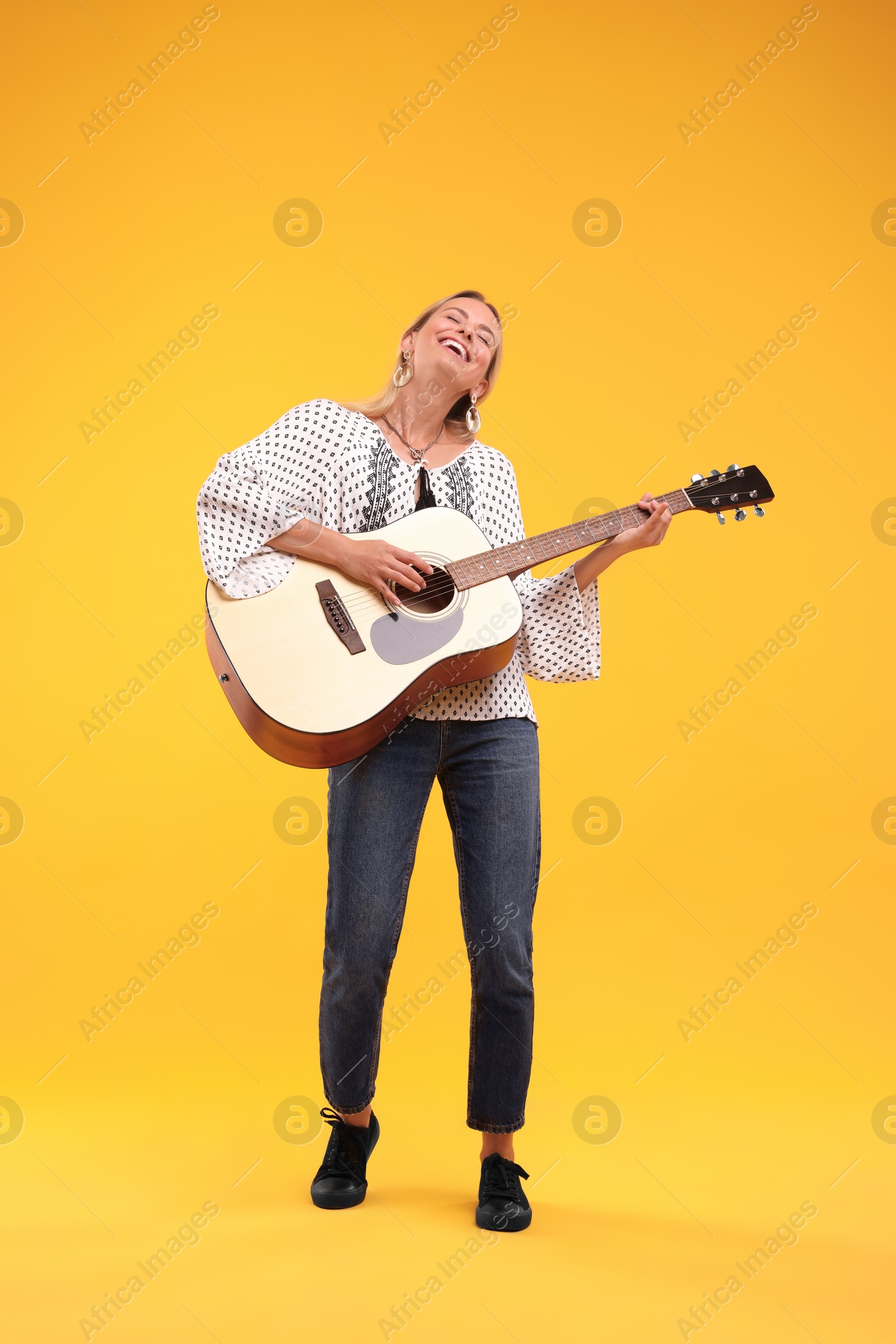 Photo of Happy hippie woman playing guitar on yellow background