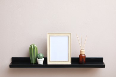 Photo of Empty photo frame, cactus figures and air reed freshener on shelf near pink wall