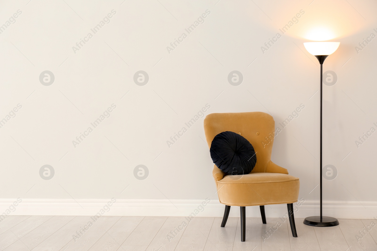 Photo of Modern floor lamp and armchair against light wall indoors. Space for text
