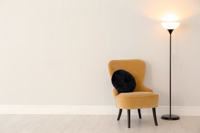 Modern floor lamp and armchair against light wall indoors. Space for text