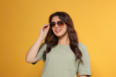 Happy beautiful woman with stylish sunglasses on orange background
