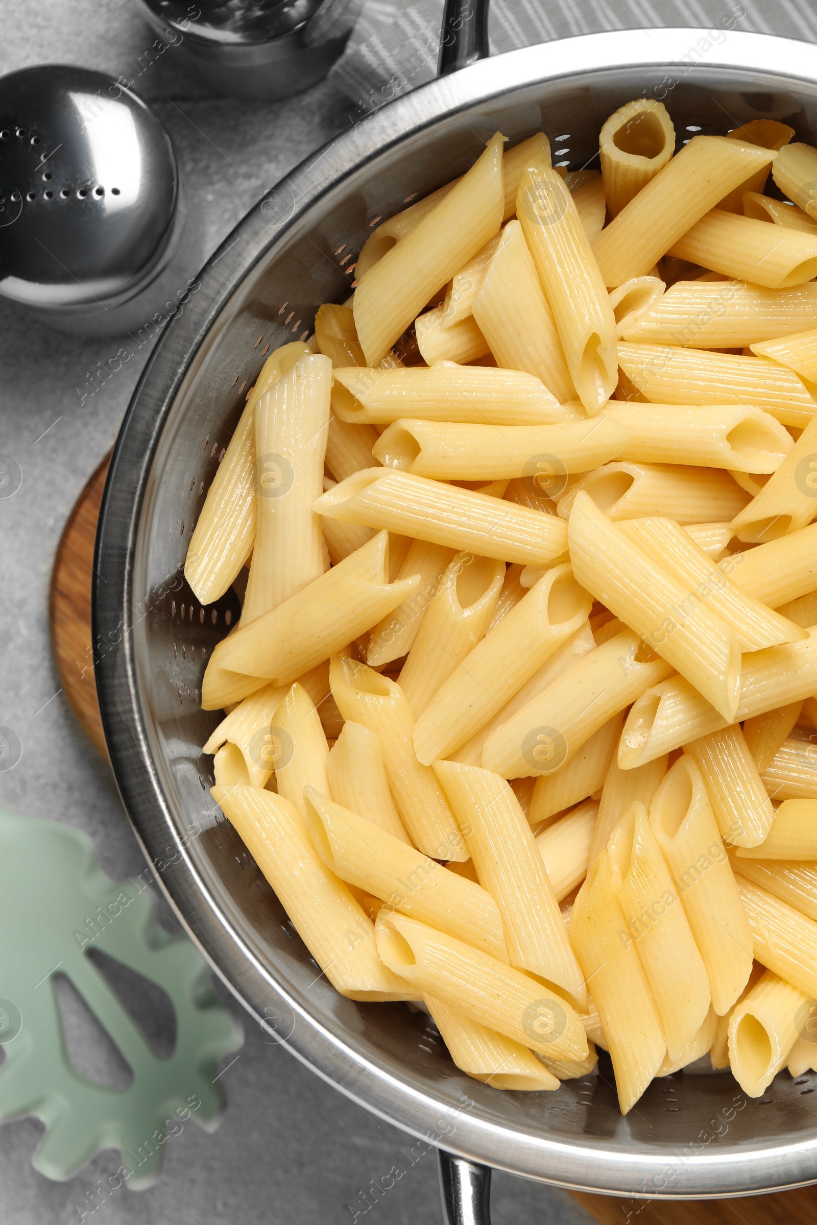 Photo of Delicious penne pasta in colander, spices and spoon on gray table, flat lay