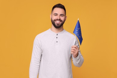 Young man holding flag of European Union on orange background