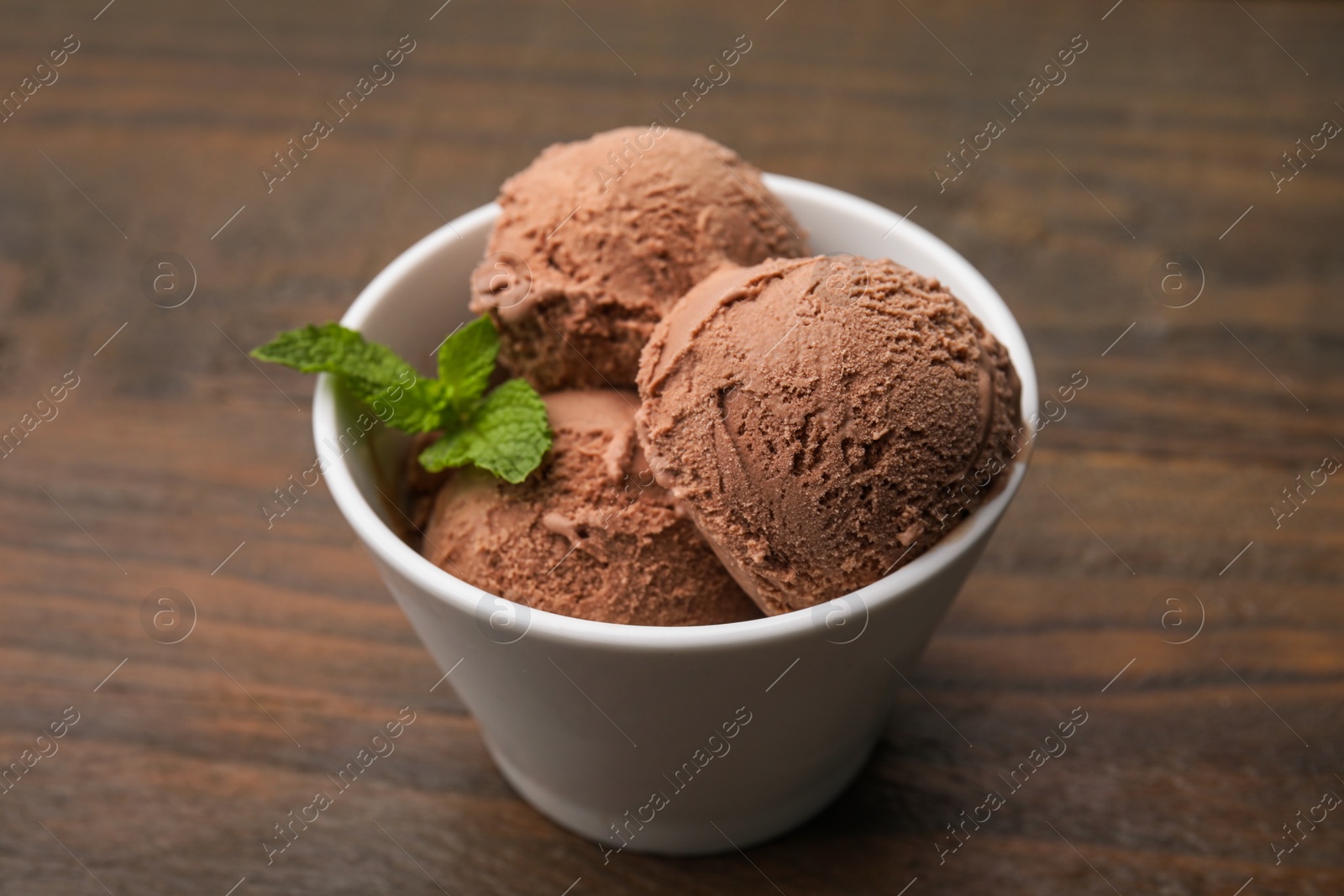 Photo of Bowl with tasty chocolate ice cream and mint leaves on wooden table