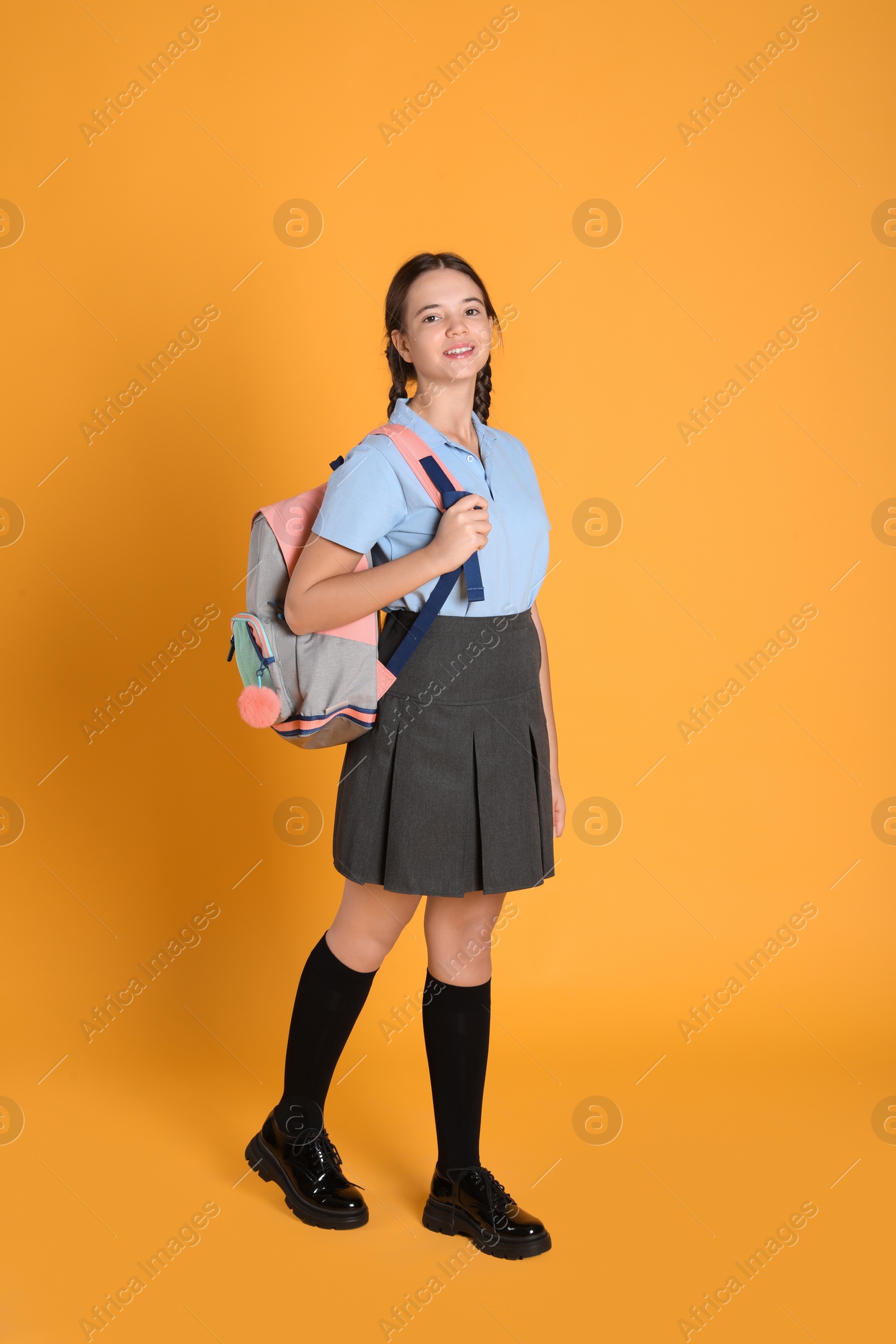 Photo of Teenage girl in school uniform with backpack on orange background