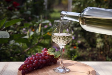 Pouring white wine from bottle into glass at wooden table outdoors, closeup. Space for text